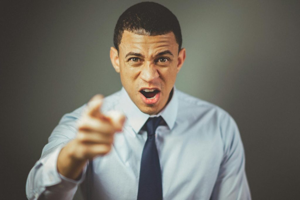 Close-up of an angry businessman in a tie expressing frustration and pointing at someone.
