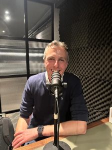 Justin Neale in front of a microphone recording a podcast about value pricing and customer experience