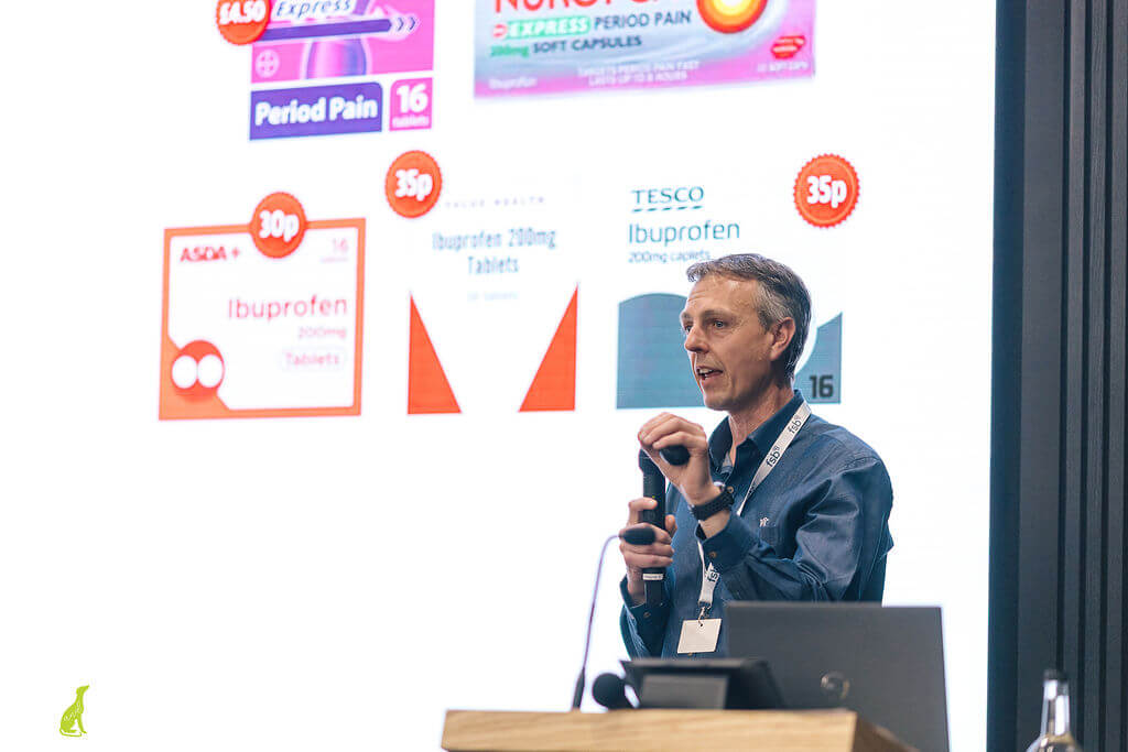 Close up of Justin Neale presenting on stage at an event with a large screen behind him